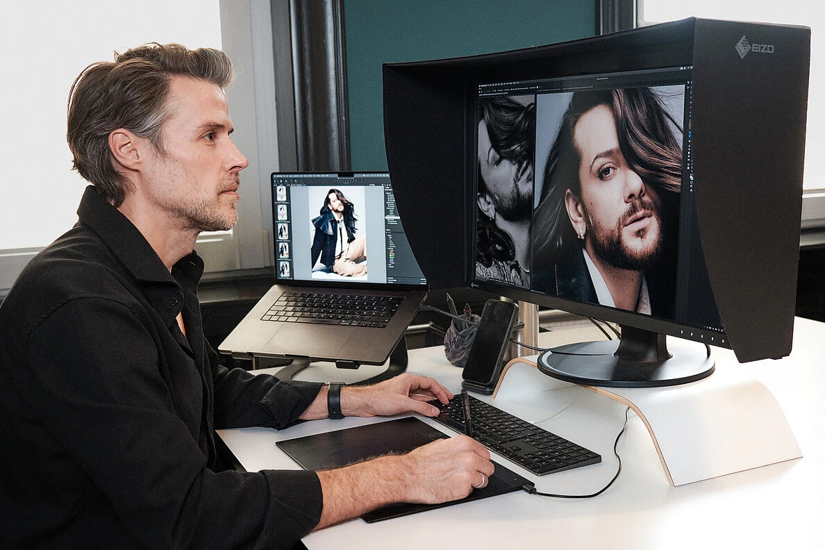 Jan Wischermann working with a pen tablet beside a hooded EIZO ColorEdge display and a laptop