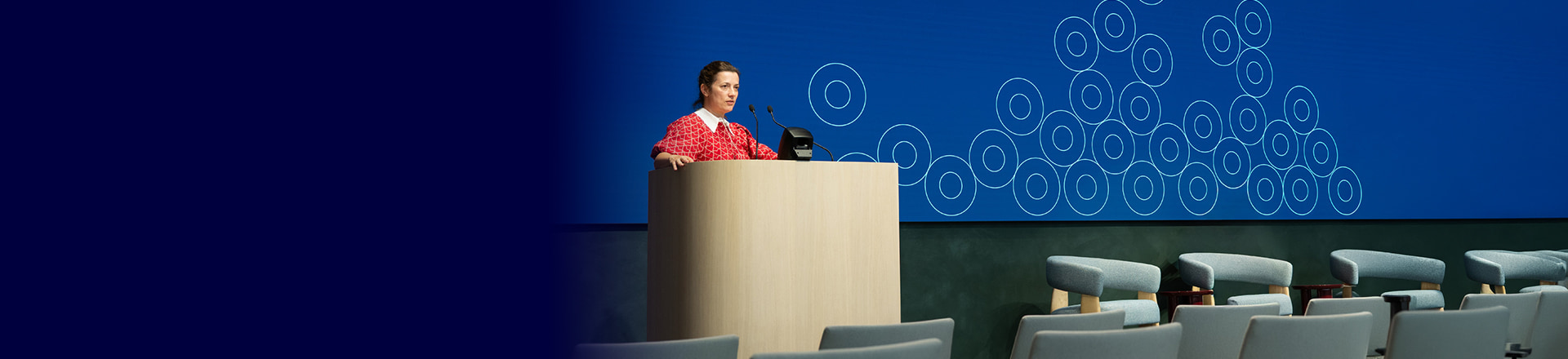 Speaker at a lectern in front of a wide blue LED display at Travers Smith